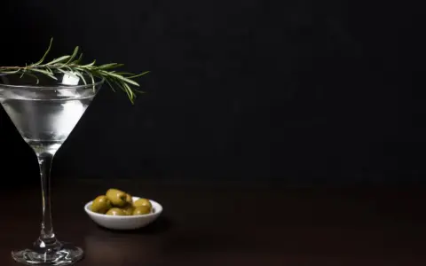 Elegancki kieliszek z drinkiem, gałązka rozmarynu i oliwki. Czy to Dirty Martini, czy klasyczne Dry Martini?