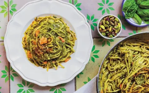 Pyszny makaron z zielonym pesto i pistacjami, wyglądający jak makaron jak z restauracji. Obok miseczka z pistacjami i listki bazylii.