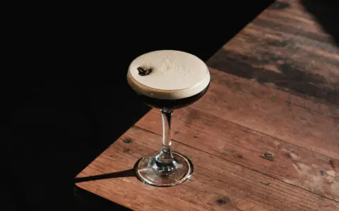 Espresso Martini przepis: elegancki koktajl z pianką i ziarnem kawy na drewnianym blacie.