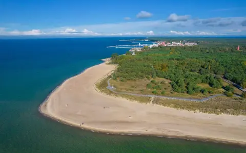 Widok z lotu ptaka na piaszczystą plażę, las i miasteczko nad morzem.