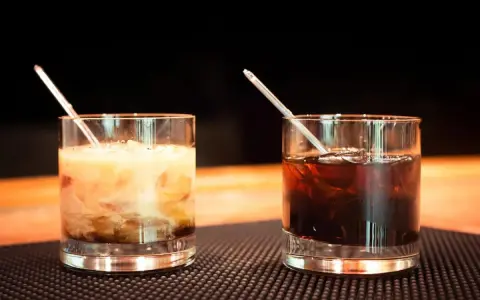 Dwa drinki z likierem kawowym na barze. Jeden kremowy, drugi ciemny, oba z lodem i słomką.