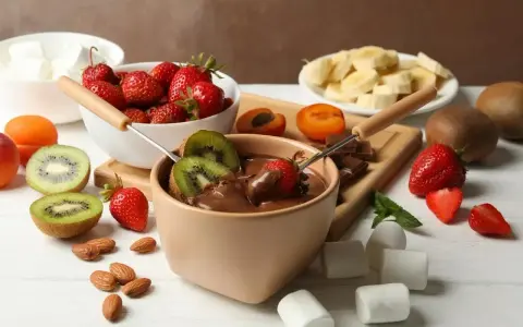 Jak zrobić fondue czekoladowe: zanurzaj truskawki i kiwi w gorącej czekoladzie. Na stole owoce, pianki i migdały.