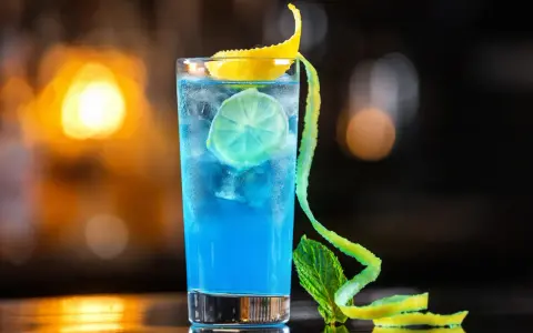 Niebieski koktajl z granatem, lodem, plasterkiem limonki i ozdobną skórką cytrynową.