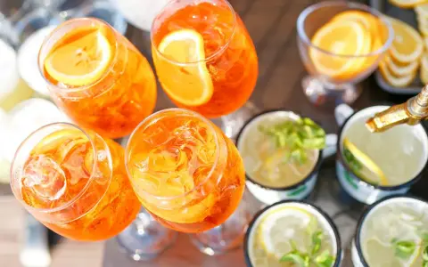 Orzeźwiający drink z prosecco, udekorowany plasterkiem pomarańczy, czeka na gości. Obok inne napoje z miętą i cytryną.