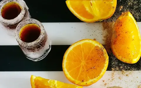 Dwa kieliszki z Jägermeisterem ze spritem, obok pokrojone pomarańcze posypane przyprawami.