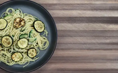Penne z cukinią na ciemnym talerzu, ozdobione grillowanymi plasterkami cukinii. Danie wygląda apetycznie i lekko.