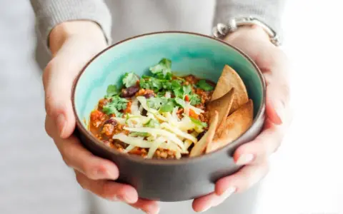 Miseczka pysznego chili con carne przepis, posypana serem i świeżą kolendrą, z chrupiącymi nachos. Idealne na chłodne dni.