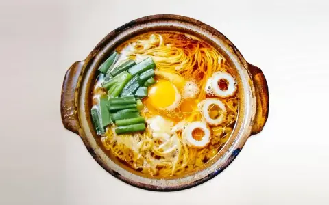 Gorący garnek z aromatycznym bulionem, żółtkiem jajka, zielonym szczypiorkiem i krążkami rybnymi. Czy to ramen czy udon?