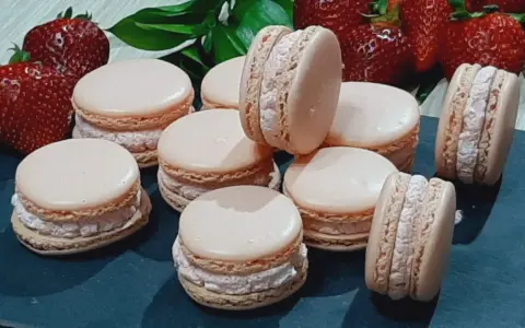 Delikatne makaroniki na mące migdałowej lub kokosowej, z kremowym nadzieniem i świeżymi truskawkami w tle.