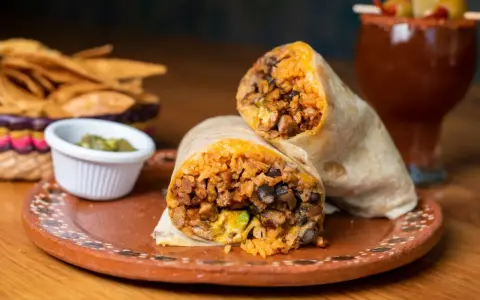 Pyszny burrito przepis: soczyste mięso, ryż, fasola i awokado zawinięte w tortillę. Obok chipsy i sos.