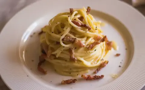 Pyszne spaghetti carbonara, idealne na prosty przepis. Kremowy sos, chrupiący boczek i czarny pieprz na talerzu.