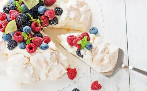 Beza Pavlova przepis: puszysta beza z bitą śmietaną i świeżymi owocami leśnymi, ozdobiona listkami mięty i plasterkami limonki.