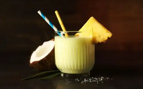 Orzeźwiający drink z mlekiem, kokosem i ananasem, ozdobiony plasterkiem owocu i kolorowymi słomkami. Idealny na tropikalne popołudnie.