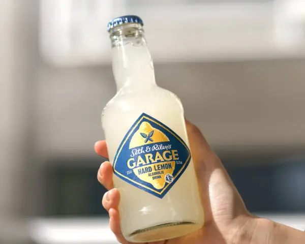 Ręka trzyma butelkę Seth & Riley's GARAGE Hard Lemon, orzeźwiający drink z piwem.