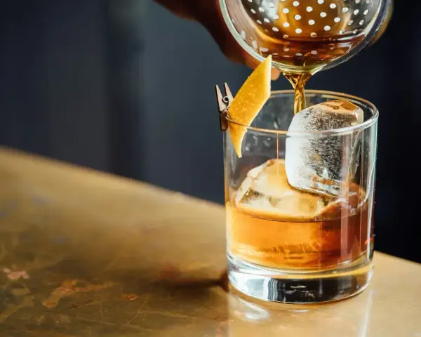 Idealny moment, by drink whisky z colą. Bursztynowy płyn z lodem i skórką pomarańczy.