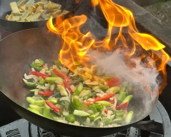 Pyszny stir-fry przepis w akcji! Warzywa w woku płoną żywym ogniem, tworząc apetyczny dym.