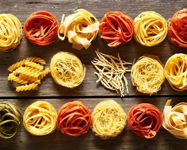 Różne rodzaje makaronu, w tym porcja makaronu spaghetti, ułożone na drewnianym blacie.