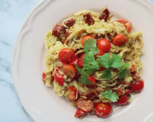 Pyszne dietetyczne spaghetti z cukinii z pomidorkami koktajlowymi i suszonymi pomidorami, udekorowane świeżą kolendrą.