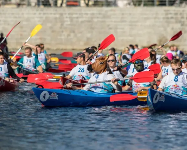 Zawodnicy w łodziach, jeden w masce konia, rywalizują w wyścigu. Wódka z Red Bullem i wódka z sokiem pomarańczowym to napoje, które mogą dodać energii.