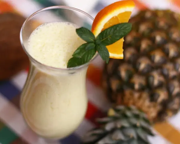 Orzeźwiający drink z ananasem, ozdobiony plasterkiem pomarańczy i miętą, na tle całego owocu.