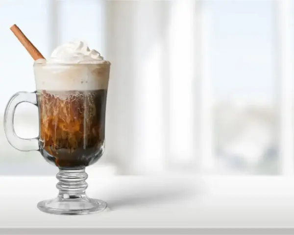 Pyszny irish coffee drink z bitą śmietaną i laską cynamonu, idealny na chłodny wieczór.