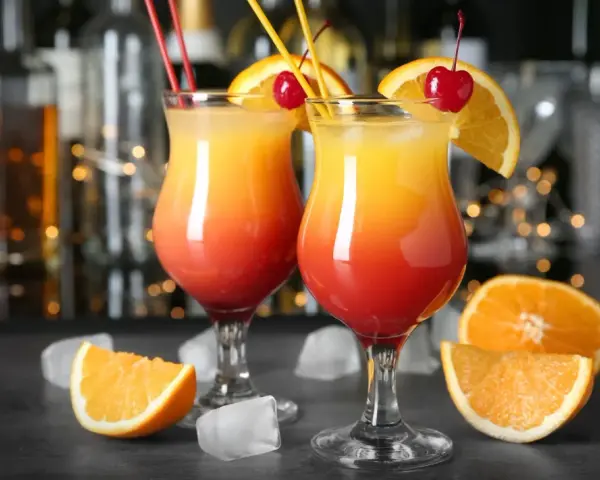 Dwa kolorowe drinki z parasolką, ozdobione pomarańczą i wiśnią, stoją na barze.