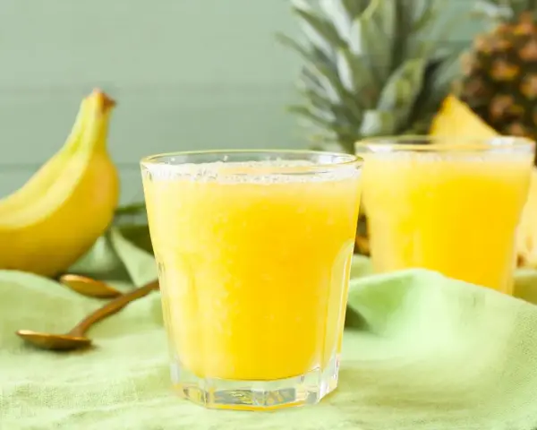 Orzeźwiający koktajl z ananasa i banana, idealny na upalne dni. Obok leżą świeże owoce i złote łyżeczki.