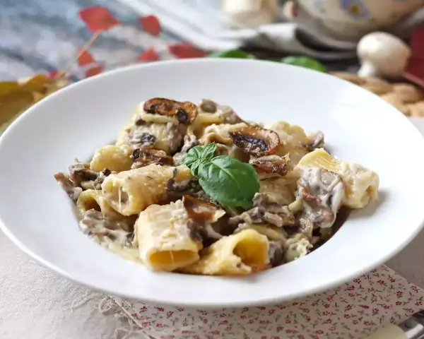 Pyszne spaghetti z grzybami w kremowym sosie, udekorowane listkiem bazylii. Idealne na jesienny obiad.