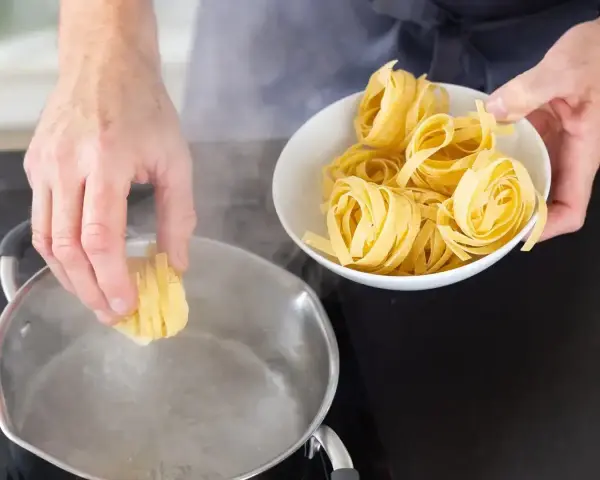 Ręka wkłada tagliatelle do wrzącej wody. Kluczowe jest, na jakim ogniu gotować makaron, by był al dente.