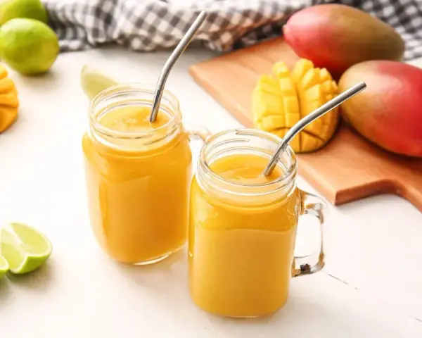 Orzeźwiający drink z wódką mango, podany w słoiczkach z metalowymi słomkami, obok świeżych owoców mango i limonek.