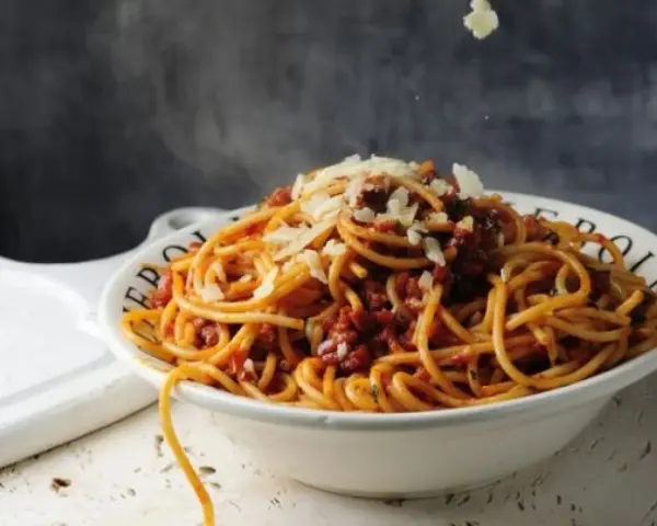Gorące spaghetti z sosem bolońskim i parmezanem, parujące w misce. Czy to bucatini czy spaghetti, smakuje wyśmienicie!