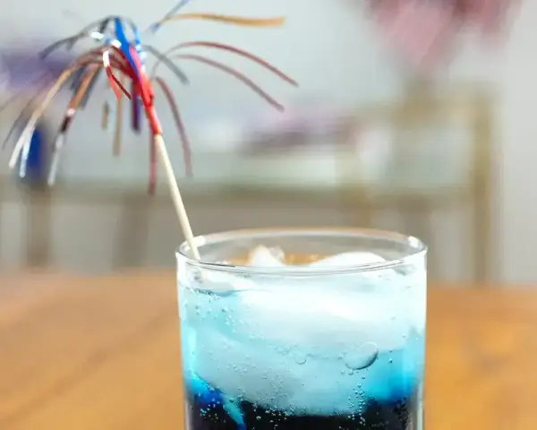 Niebieski drink z lodem i parasolką, przypominający letni koktajl z blue curacao.
