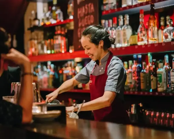 Uśmiechnięta barmanka przygotowuje drinki za ladą pełną alkoholi. Ciekawe, ile zarabia barman w Turcji?