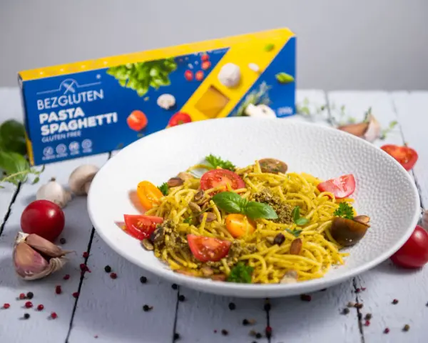 Pyszny talerz makaronu spaghetti bezglutenowego z pesto, pomidorkami i migdałami. Obok pudełko makaronu.