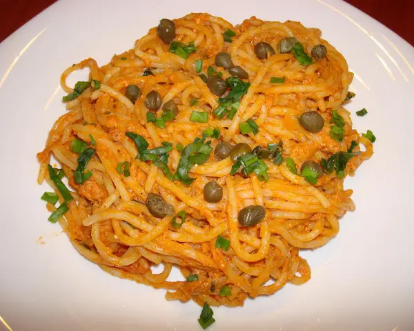 Pyszne spaghetti z tuńczykiem i kaparami, posypane szczypiorkiem, na białym talerzu.