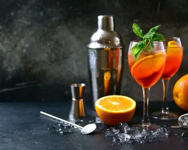 Orzeźwiający aperol z szampanem, udekorowany pomarańczą i miętą, gotowy do podania. Obok shaker i akcesoria barmańskie.