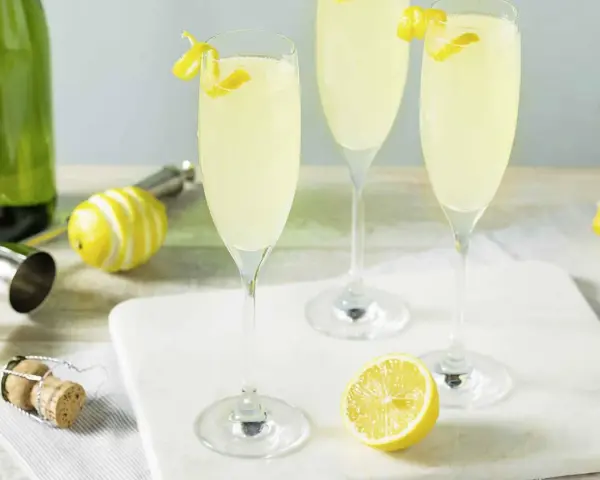 Trzy kieliszki musującego drinka French 75, jeden na ginie, drugi na koniaku, z cytrynową dekoracją.