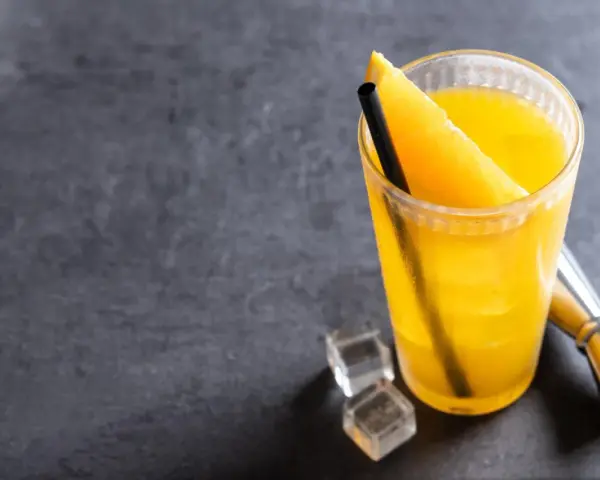 Orzeźwiający drink z wódką i sokiem pomarańczowym, ozdobiony plasterkiem pomarańczy, z kostkami lodu i miarką barmańską obok.