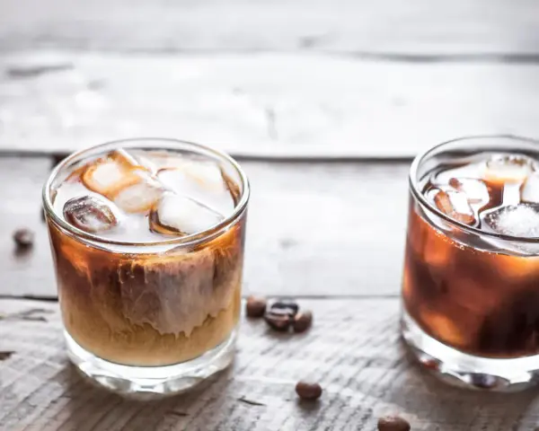 Dwa drinki na drewnianym blacie: jeden to White Russian, drugi to Black Russian.