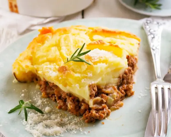 Pyszna zapiekanka pasterska (Shepherd's Pie) z warstwą mielonego mięsa i kremowym purée ziemniaczanym, ozdobiona gałązką rozmarynu.