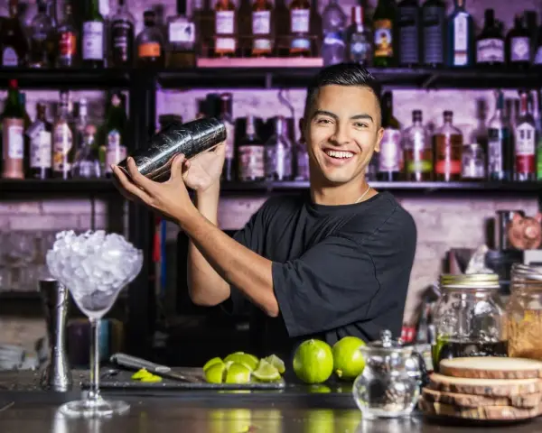 Uśmiechnięty barman miesza drinka. Chcesz wiedzieć, jak zostać barmanem kobietą? Zacznij od nauki sztuki miksowania!