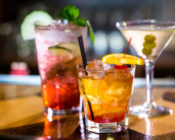 Kolorowe drinki z wódką smakową: czerwony z ogórkiem i miętą, bursztynowy z pomarańczą i wiśnią, oraz martini z oliwkami.