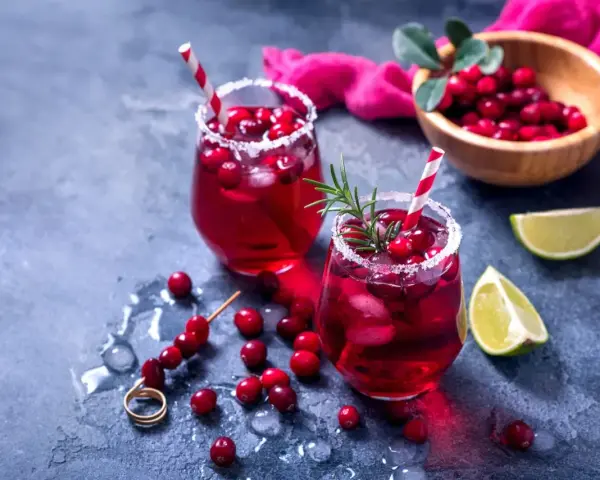 Dwa orzeźwiające drinki z grenadiną, ozdobione żurawiną i rozmarynem, z limonką w tle.