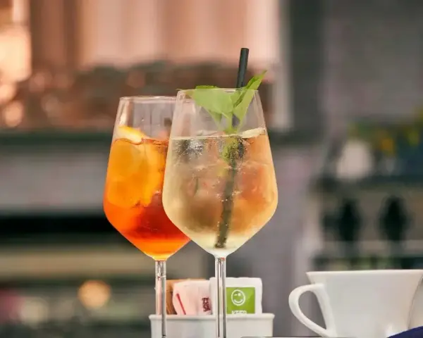 Dwa orzeźwiające drinki: pomarańczowy Aperol Spritz i zielony Hugo, gotowe do degustacji.