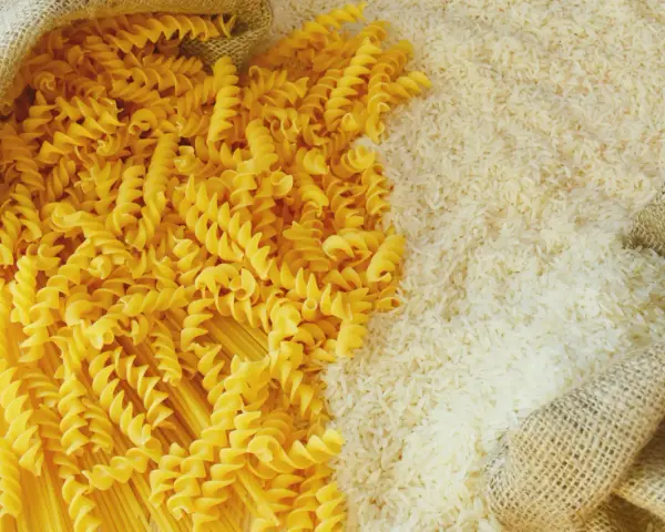Ryż vs makaron: obok siebie leżą dwa rodzaje produktów. Z worka wysypano biały ryż, a obok niego spiralne fusilli i długie spaghetti.