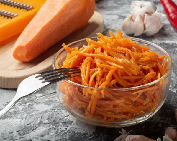 Pyszna surówka z marchewki jak z restauracji, gotowa do podania. Obok marchewka, tarka, czosnek i papryczka chili.