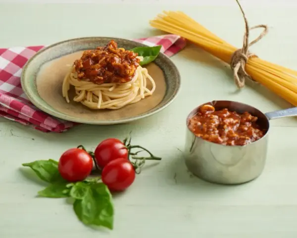 Pyszne spaghetti z sosem bolońskim, przygotowane z pomocą przyprawy do spaghetti Knorr. Obok świeże pomidory i bazylia.