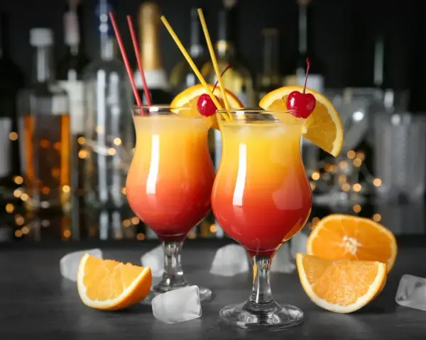 Dwa drinki z wódką, ozdobione pomarańczą i wiśnią, z kostkami lodu i owocami na blacie.