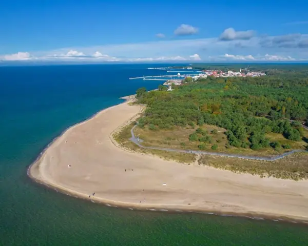 Widok z lotu ptaka na piaszczystą plażę, las i miasteczko nad morzem.