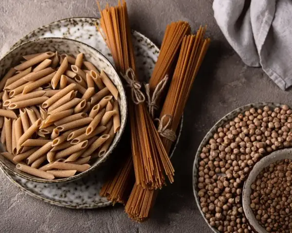Jasny makaron penne w misce i ciemny makaron spaghetti na talerzu, obok ciecierzycy.